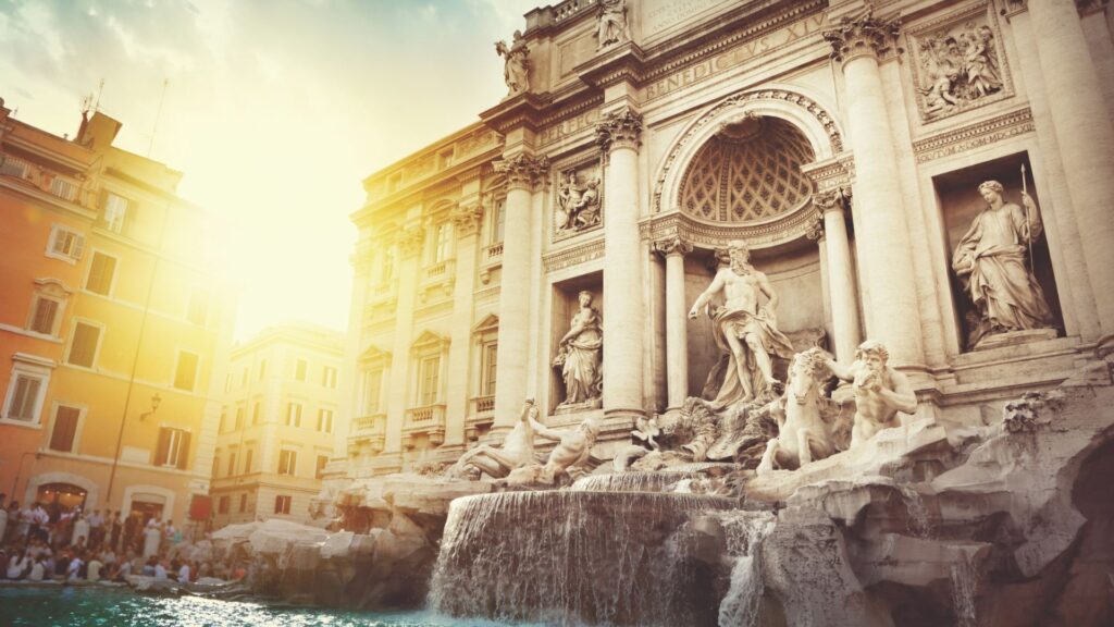 The Trevi Fountain in Rome, Italy, is shown at sunrise. Water flows from the ornate baroque structure, surrounded by statues and historic buildings, with sunlight streaming from the left—capturing the timeless beauty unique to Rome.
